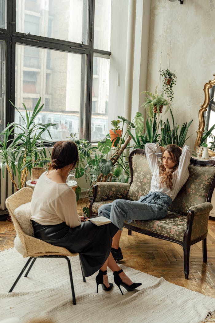 Home Two women engaged in a counseling session in a cozy, plant-filled living room.
